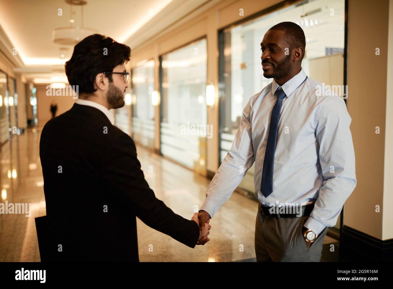 Side view portrait of two businessmen shaking hands in office building ...