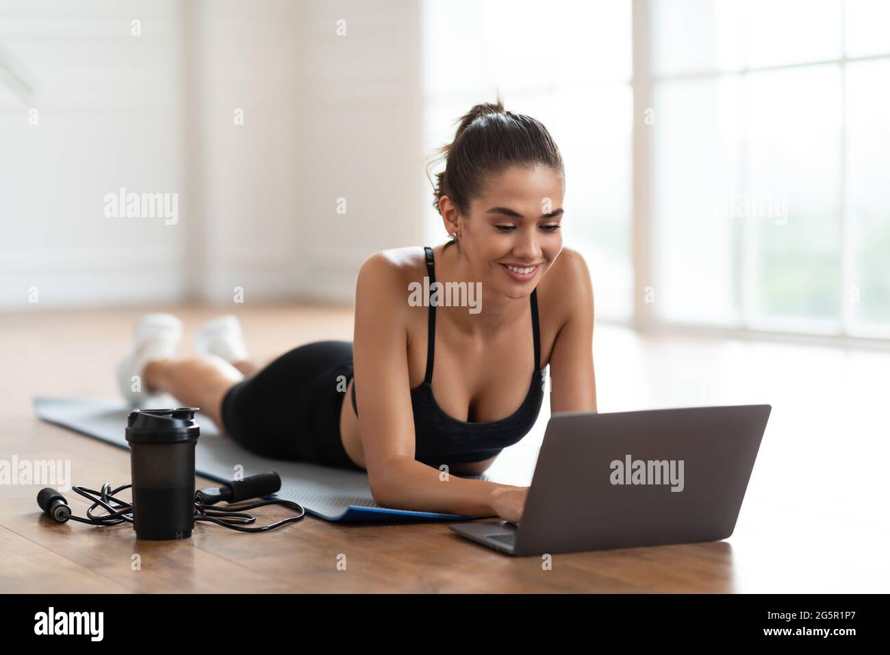 Young woman lying on yoga mat using laptop Stock Photo - Alamy