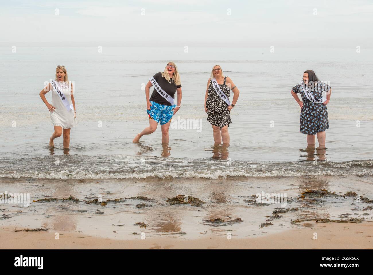 St Andrews, Fife, UK.  Soon-to-be University of St Andrews graduates Yvonne Smith, Audrey Field, Katrina Peattie and Sarah Ramage celebrating with a paddle in the North Sea.  The foursome graduate as part of the Scottish Wider Access Programme.  SWAP East is a partnership between colleges and universities in the east of Scotland that aims to promote and support access to higher education for adults.  Over 1900 students will be conferred their degrees virtually this week due to Covid-19 restrictions. Photo by Gayle McIntyre Stock Photo