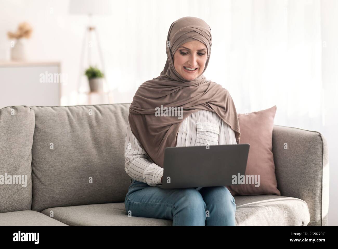 Mature Middle-Eastern Woman Using Laptop Browsing Internet Sitting At Home Stock Photo
