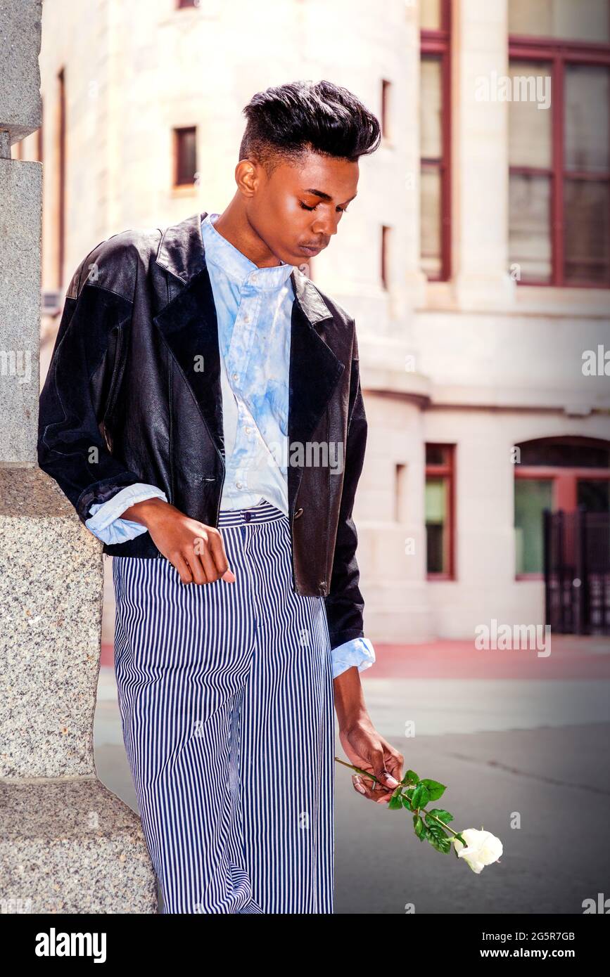 Lonely boy. A 18 years old student, wearing a fashionable black jacket, striped pants, a blue-dyed white shirt, is standing by the gate on campus, hol Stock Photo