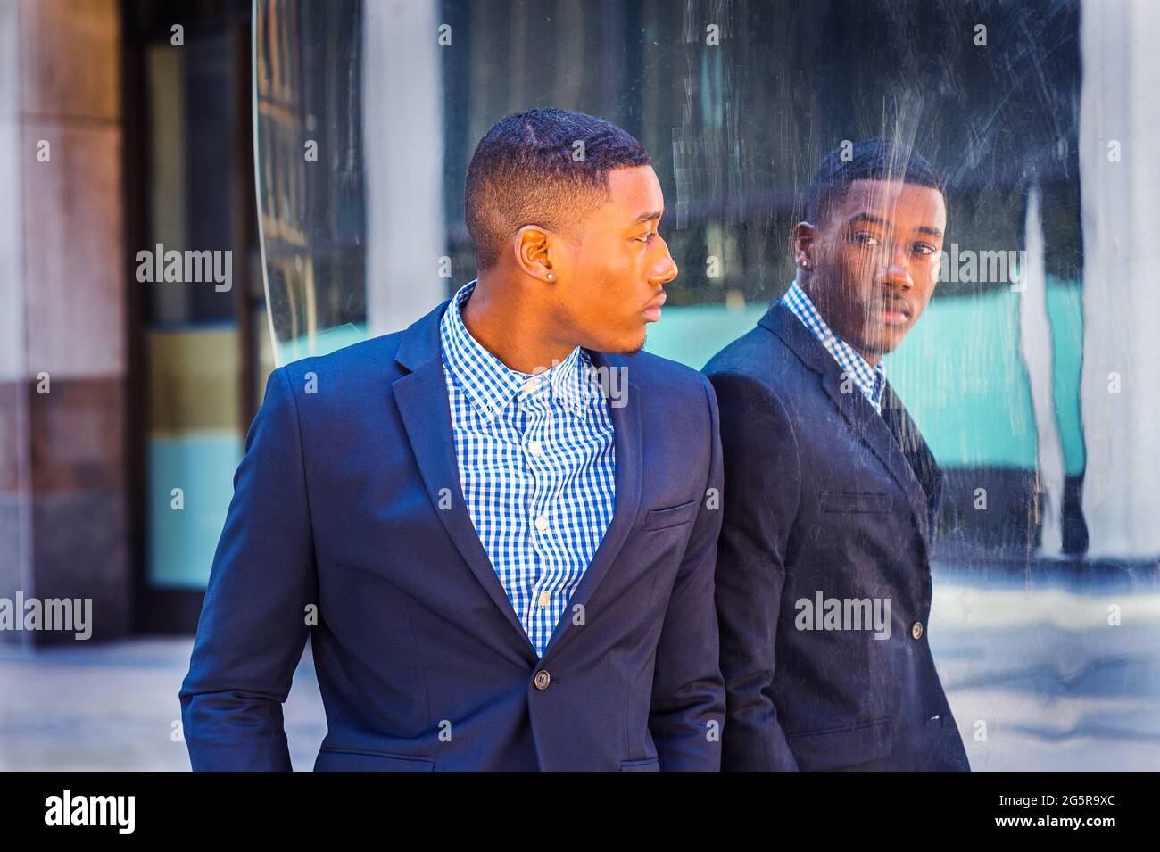 A young black businessman is standing by a mirror on the street and looking at the reflection. Concept of self assured, self esteem and self checking. Stock Photo
