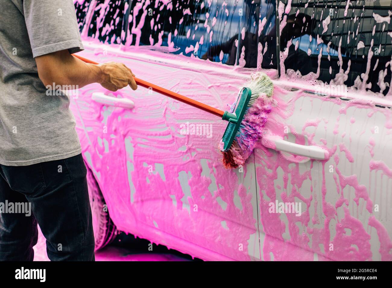 Worker washing a white car with a brush, at a car wash, a man