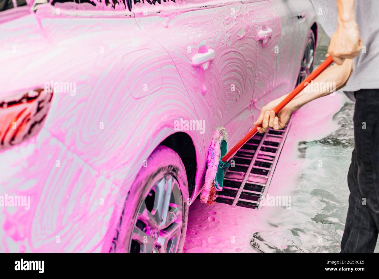 Worker washing a white car with a brush, at a car wash, a man cleans up