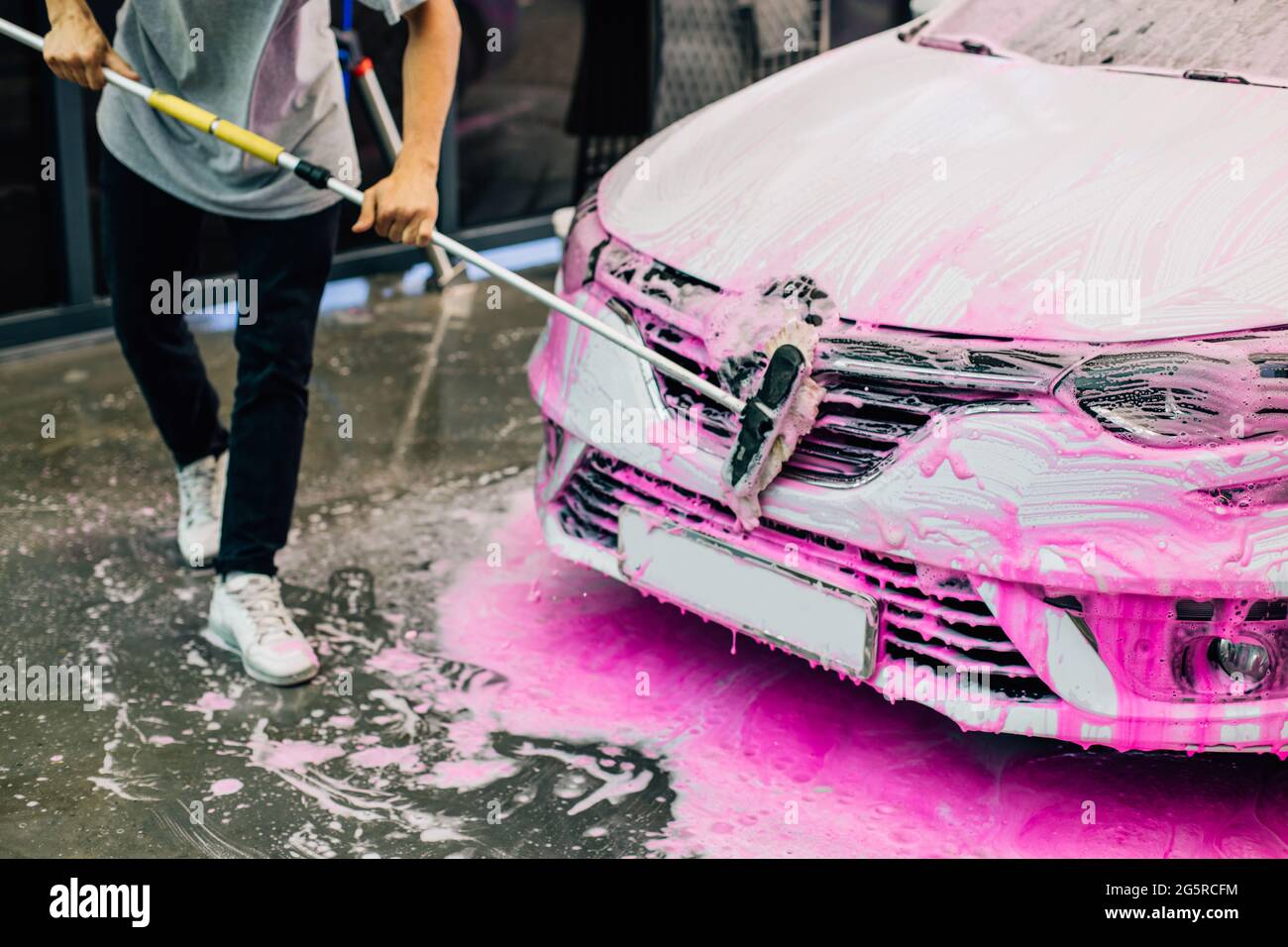 Worker washing a white car with a brush, at a car wash, a man cleans up