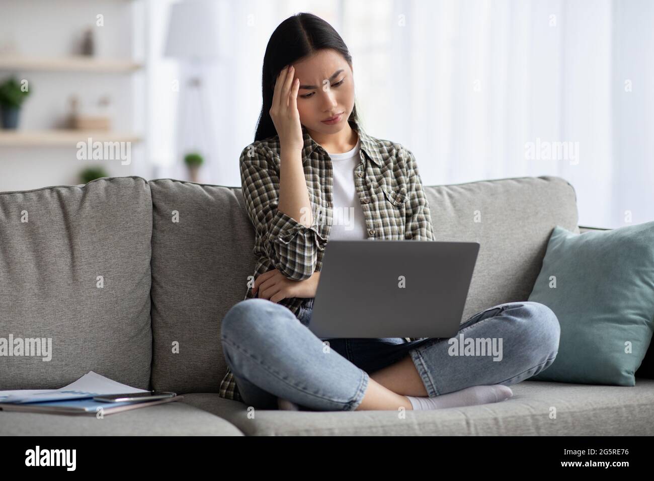 Exhausted korean lady suffering from headache while using laptop Stock Photo