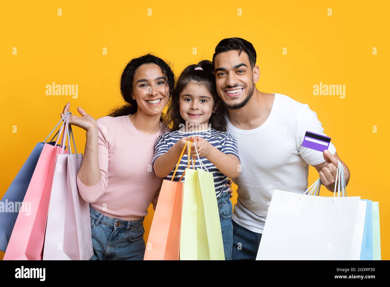 Cheerful Arab Parents And Little Daughter Holding Shopping Bags And Credit Card Stock Photo