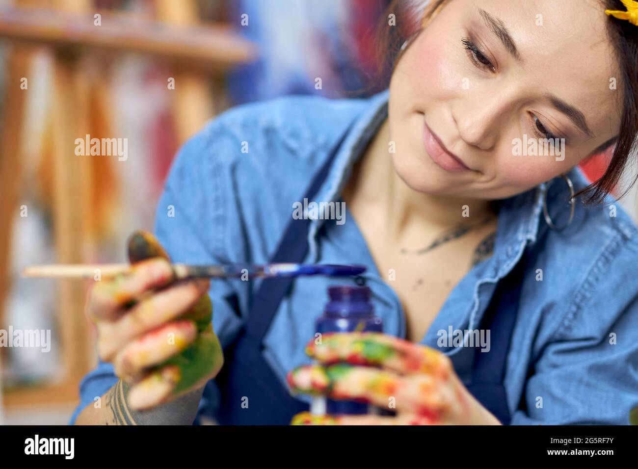 Portrait of young woman, female painter in apron holding blue paint jar ...