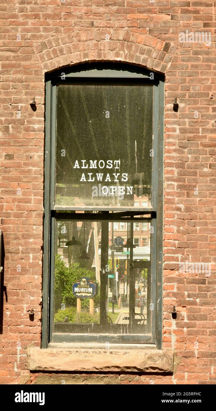 Window on a red brick building with the sign saying in white lettering, Almost Always Open. Stock Photo