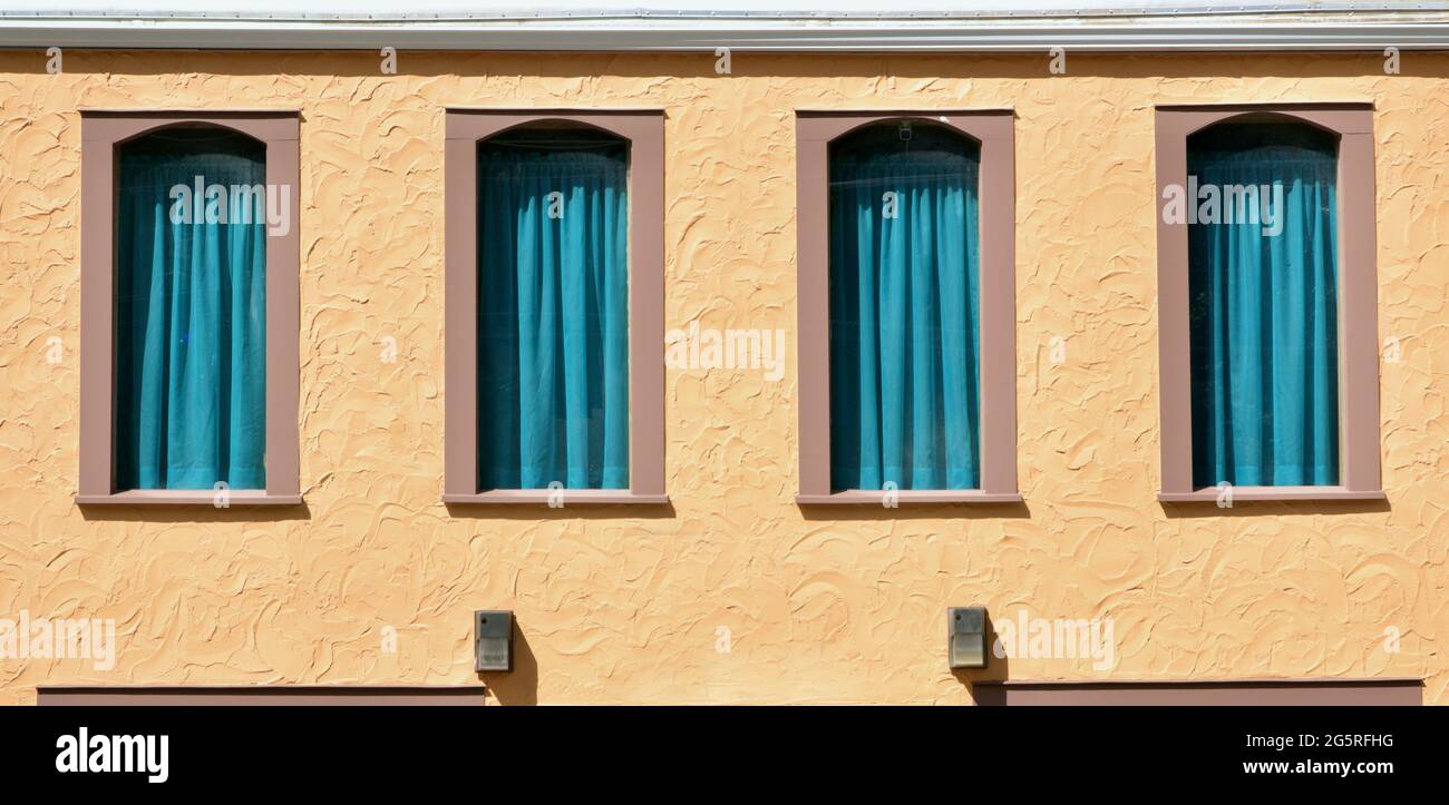 Four Shadowed Windows with Teal Blue Window Coverings with Teal Blue Flowing Curtains on a Terra Cotta colored Stucco Building. Stock Photo