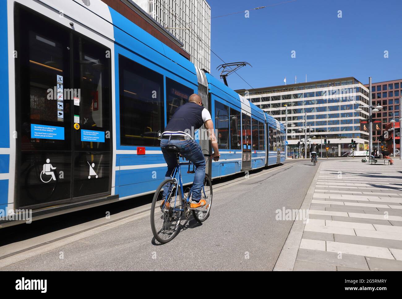 Stockholm, Sweden - May 12, 2021: A man is cycling in central Stockholm next to a modern tram on line 7 at the Sergels torg square. Stock Photo