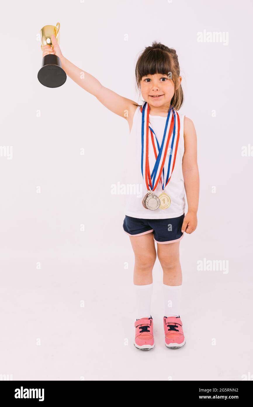 Little brown-haired girl with sports champion medals, lifting a trophy with  one hand. Sport and victory concept Stock Photo - Alamy