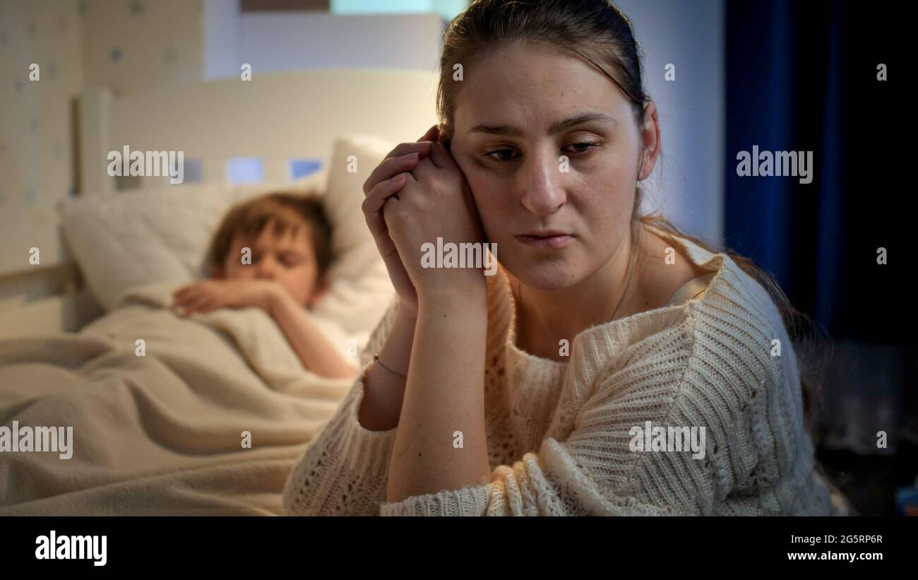 Upset And Stressed Mother Crying Next To Bed Of Her Little Son Sleeping ...