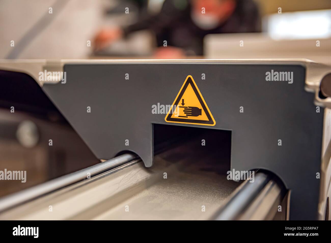 A warning sign on a woodworking machine. Production safety in a carpentry workshop. Hazard sign of moving parts in yellow triangle with hands Stock Photo