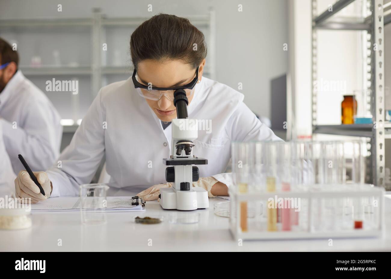 Scientist looking in microscope and taking notes while working in microbiology laboratory Stock Photo