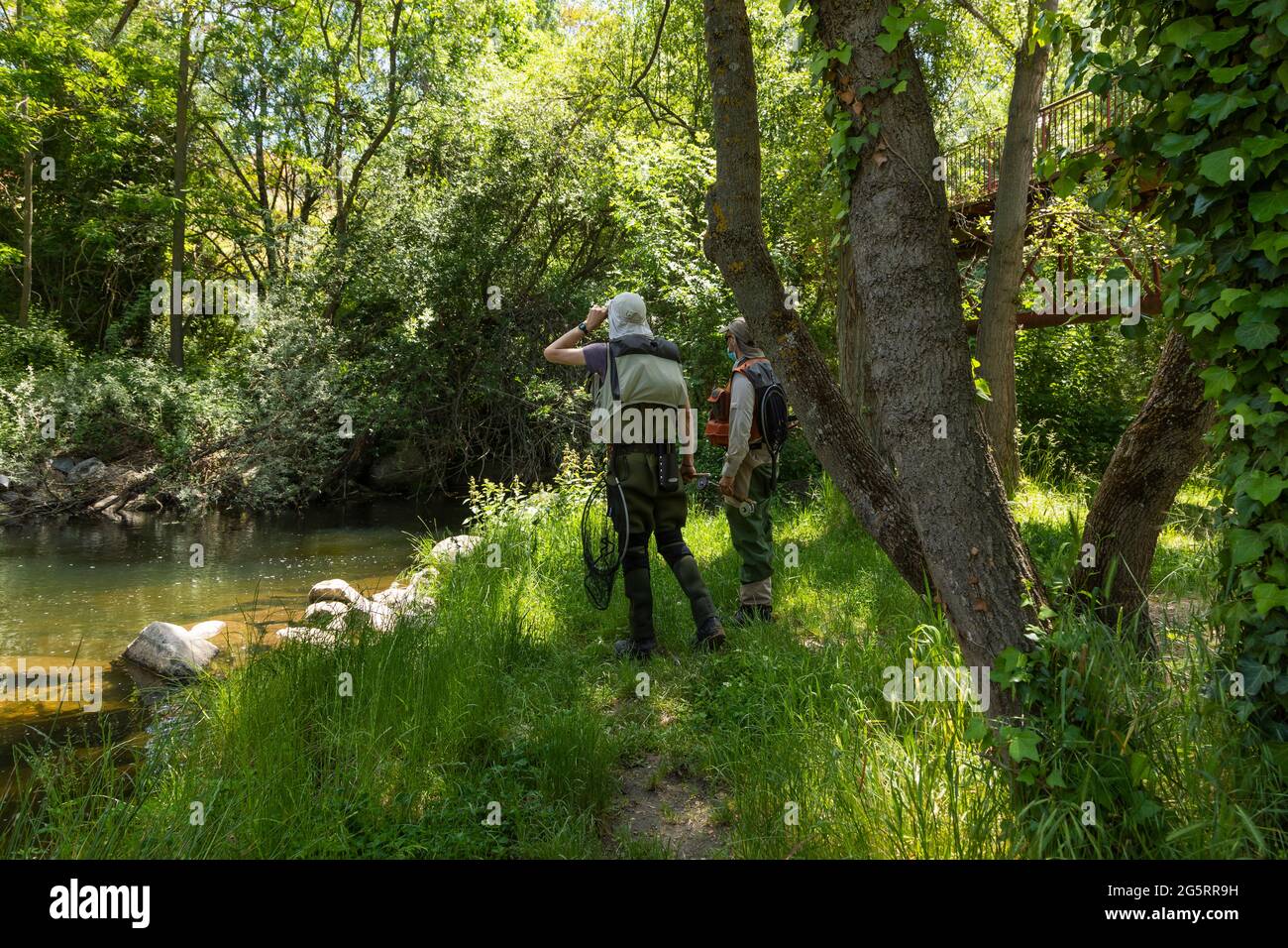 Segovia, Spain - June 2, 2021: Two fishermen look for a good fishing spot in the Eresma river, as they pass through Segovia on the Senda de los Molino Stock Photo
