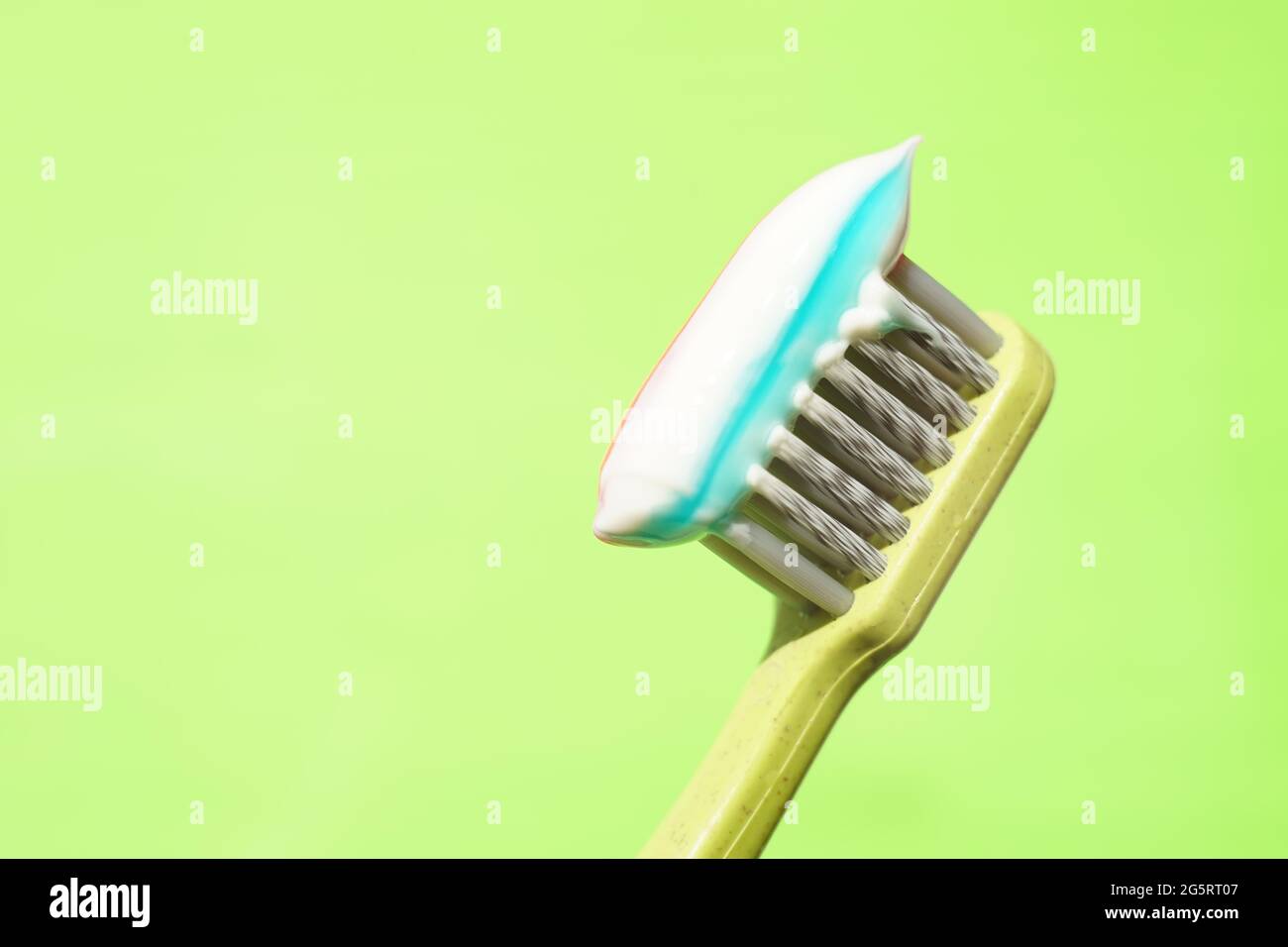 Green plastic toothbrush with striped toothpaste on green background ...