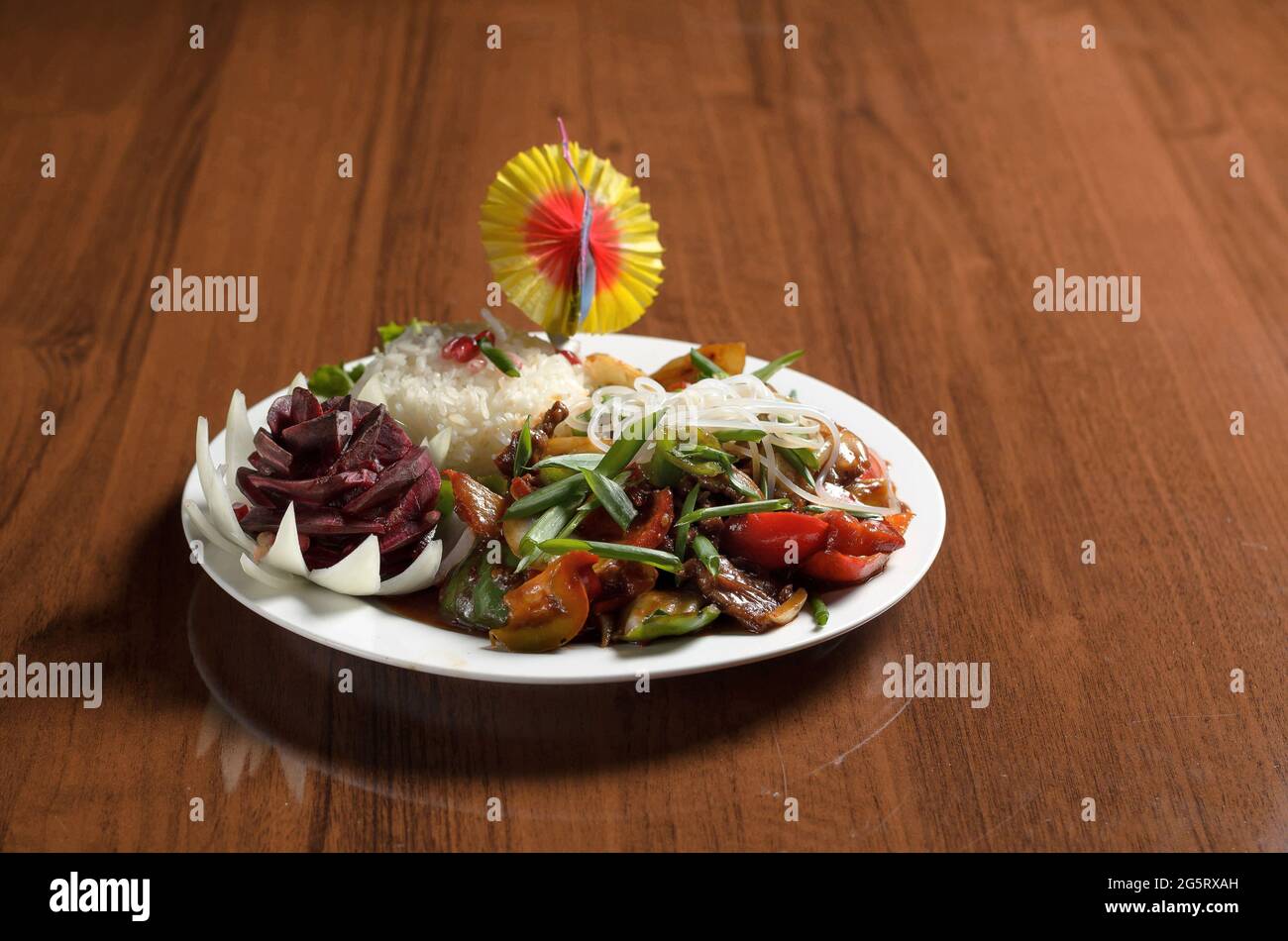 Uyghur Asian food stewed meat with vegetables, red bell pepper, tomatoes, cabbage, carrots in a white plate with rice on the table Stock Photo