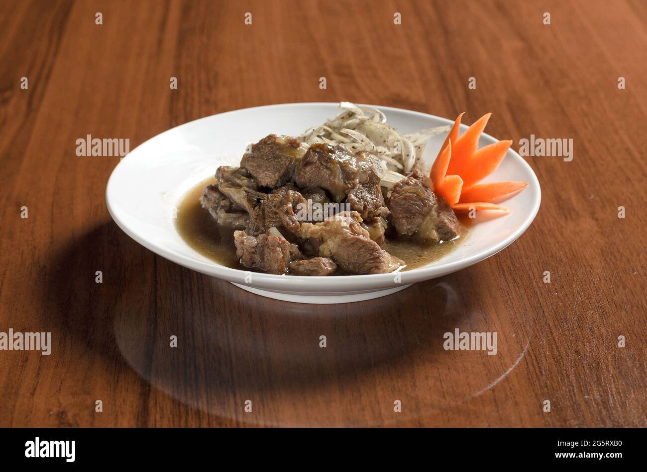 Asian cuisine Uzbek food, stewed juicy lamb meat in pieces in a white plate with onions on the table Stock Photo