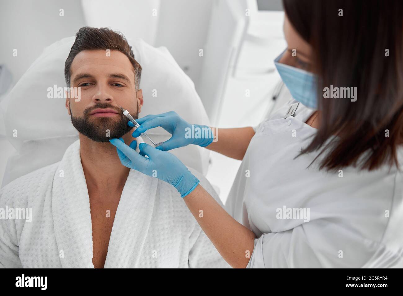Happy man with beard undergoes nasolabial fold filler procedure in cosmetology clinic Stock Photo