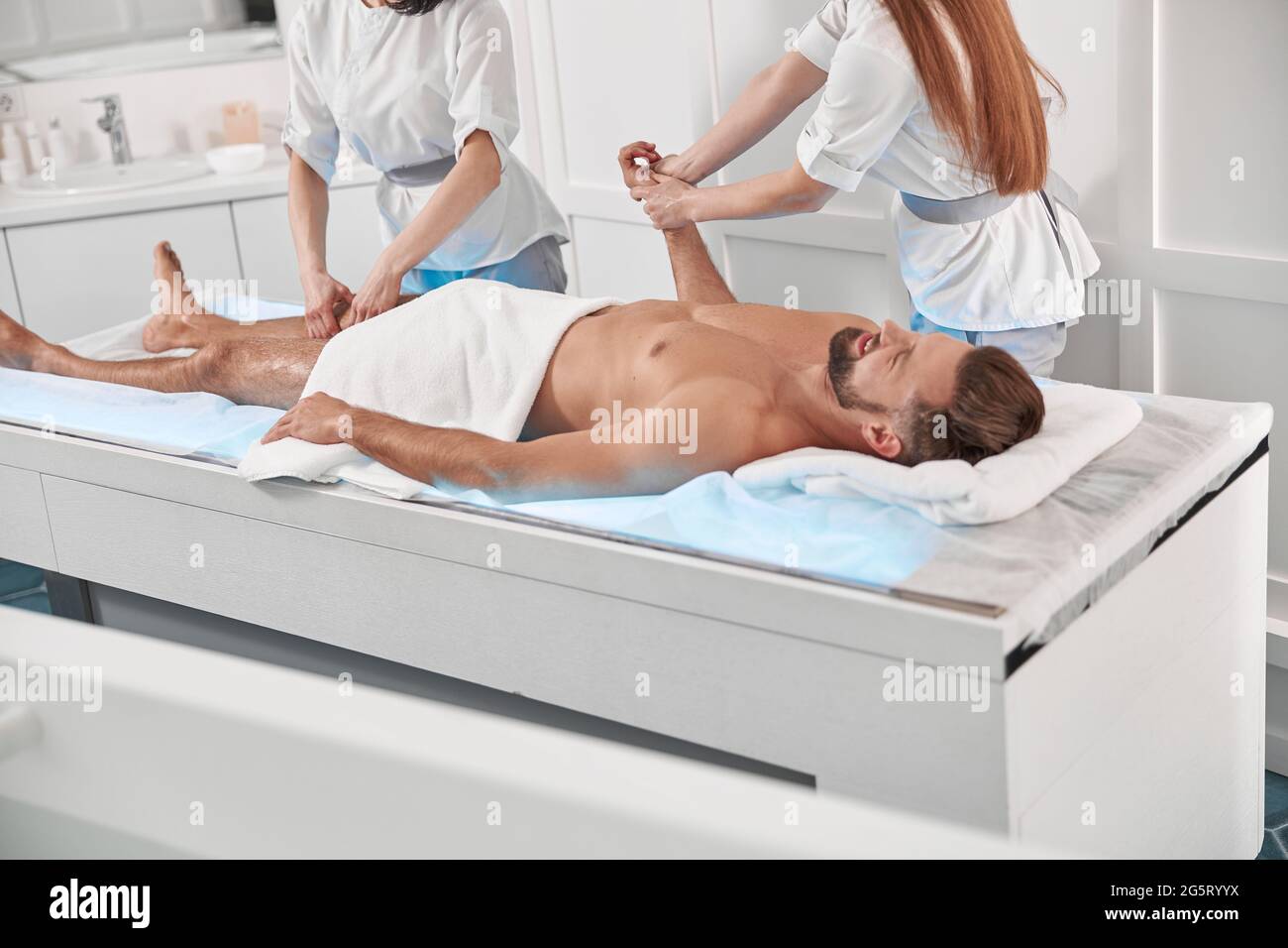 Careful chiropractics do relaxing massage to man patient lying on glowing couch in clinic Stock Photo