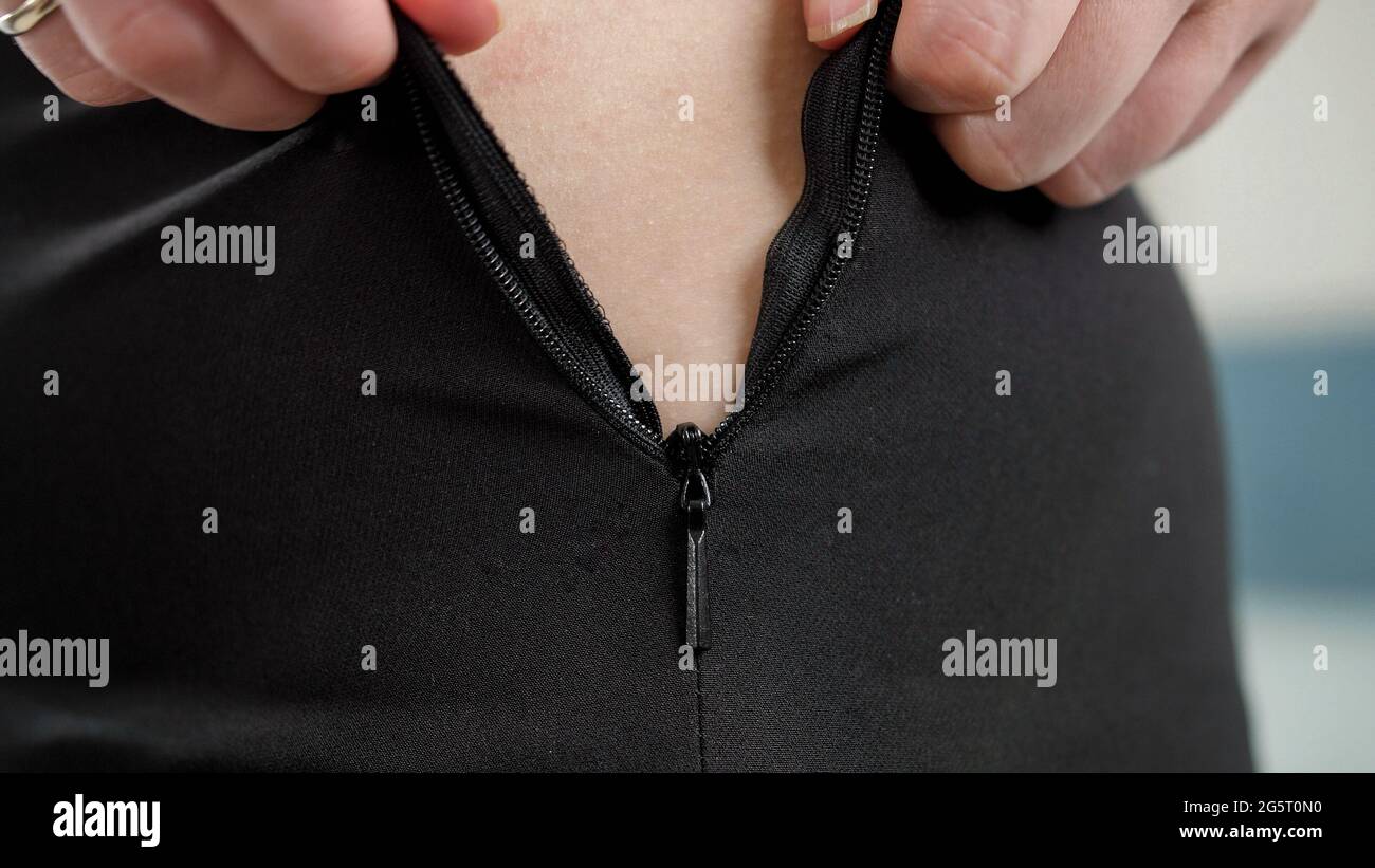 CLoseup of woman pulling stuck zipper on small tight dress. Concept of excessive weight, obese female, dieting and overweight problems Stock Photo