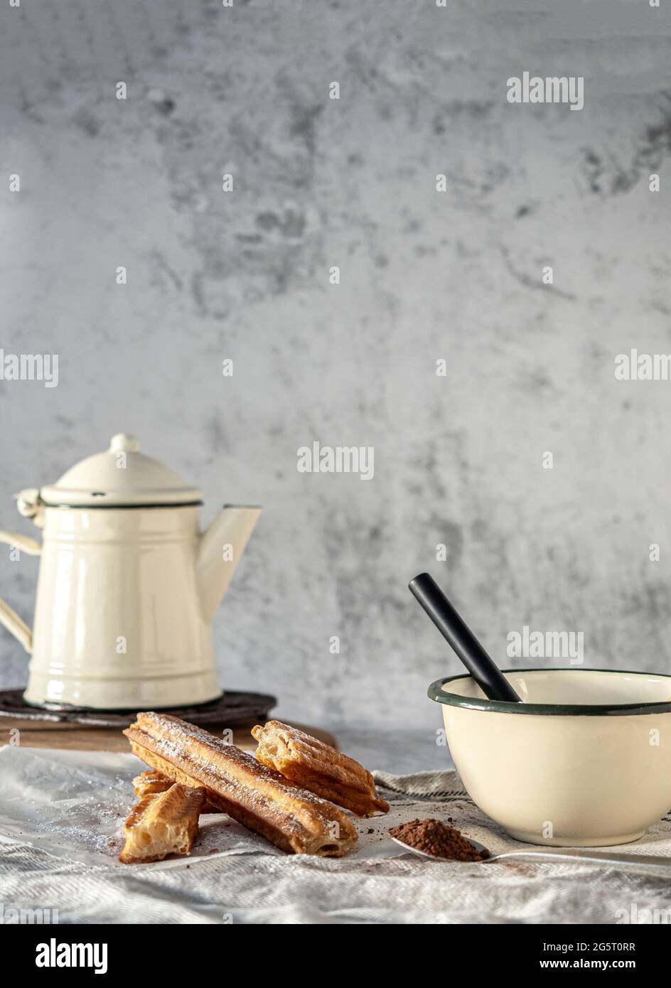 Typical Spanish breakfast or snack. Churros in paper bag with sugar. Cup with chocolate and spoon with cocoa. White background. Stock Photo