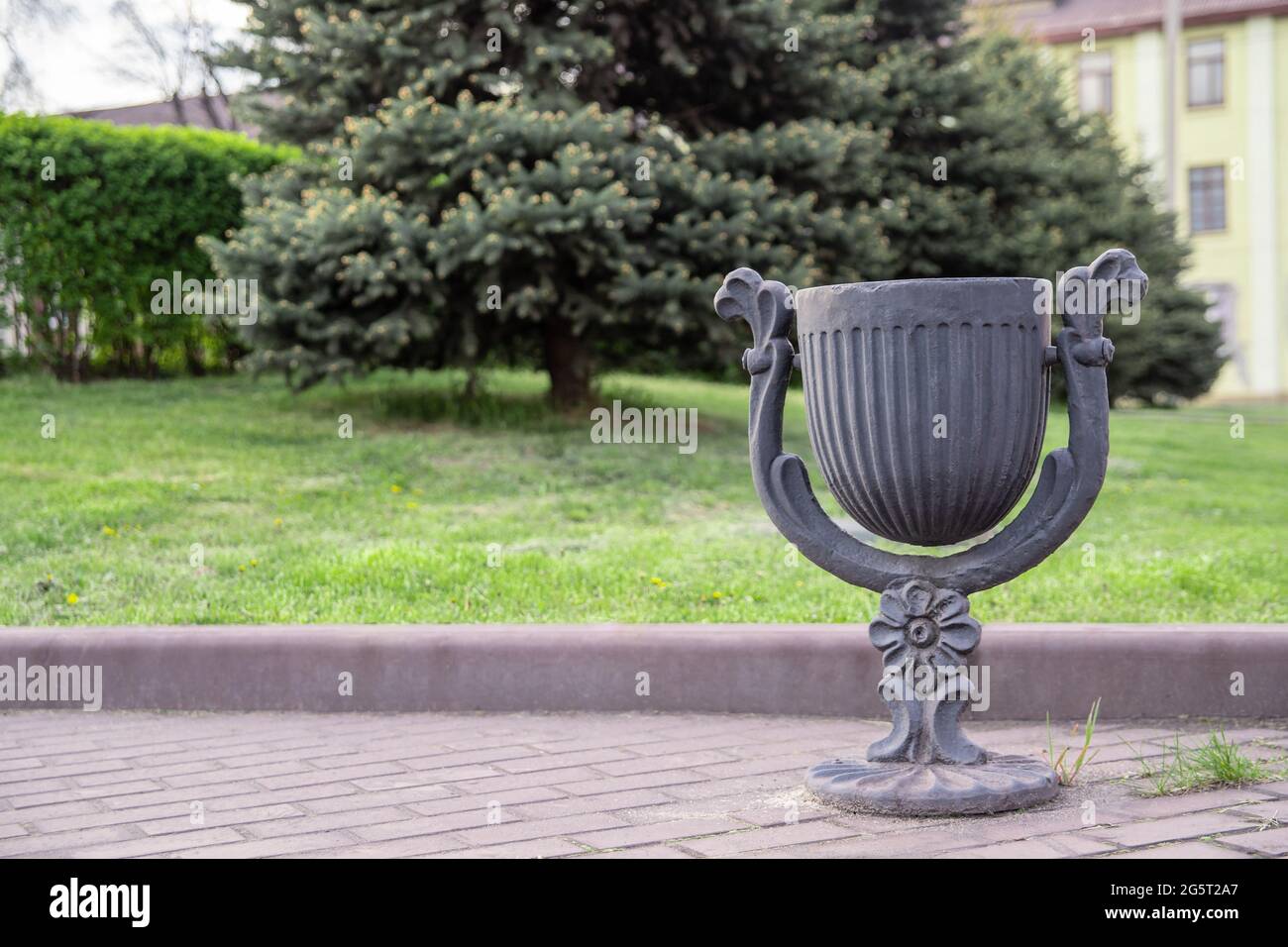 Metallic gray garbage container at the footpath in the city park. The trash bin stands in the park near the lawn against the background of nature.  Stock Photo