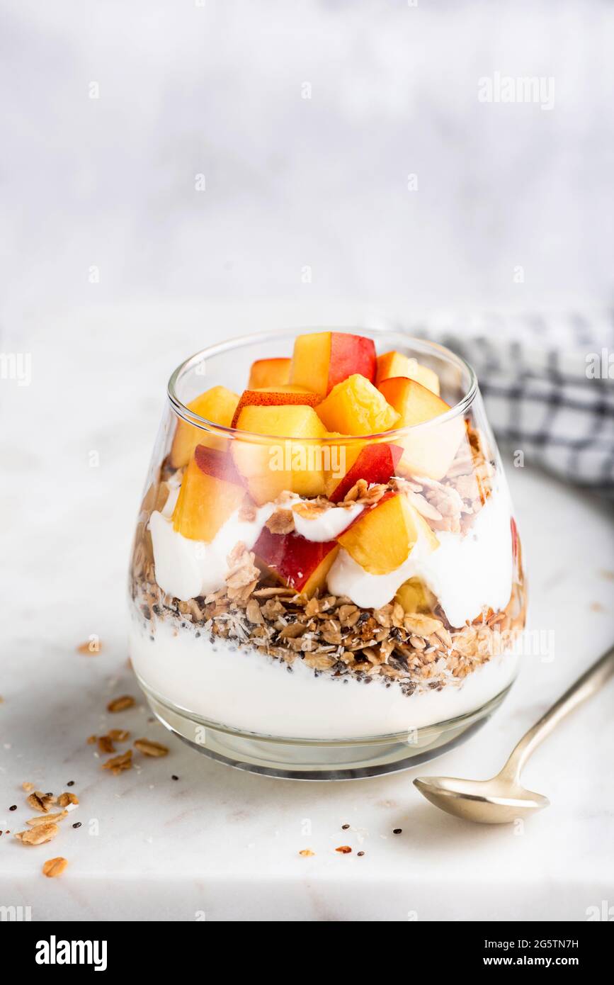 Greek yogurt granola parfait with peaches in glass on white marble