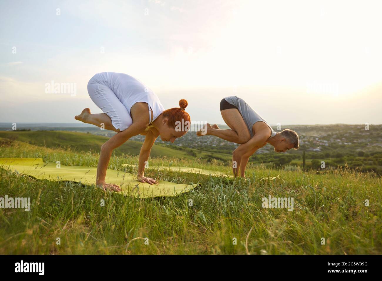 Couple doing bakasana position and practicing yoga together on nature outdoors Stock Photo