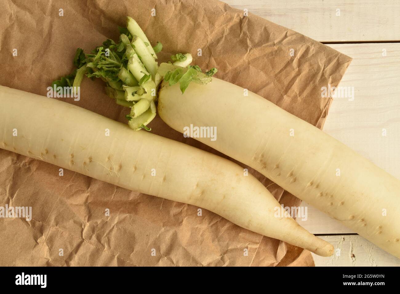 Two ripe organic radishes on brown paper, close-up, on a white wooden table, top view. Stock Photo