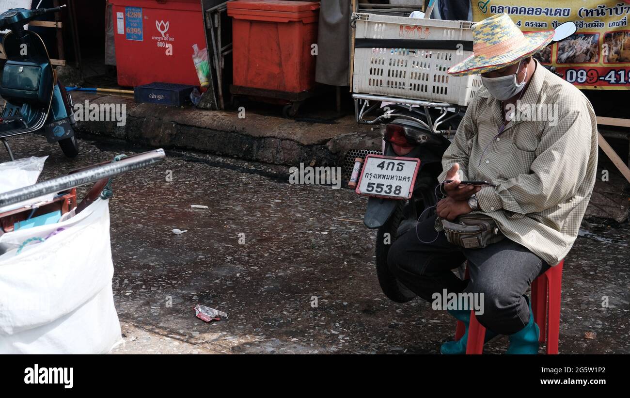 Man sitting in a chair wearing a straw hat Klong Toey Market Wholesale Wet Market Bangkok Thailand largest food distribution center in Southeast Asia Stock Photo