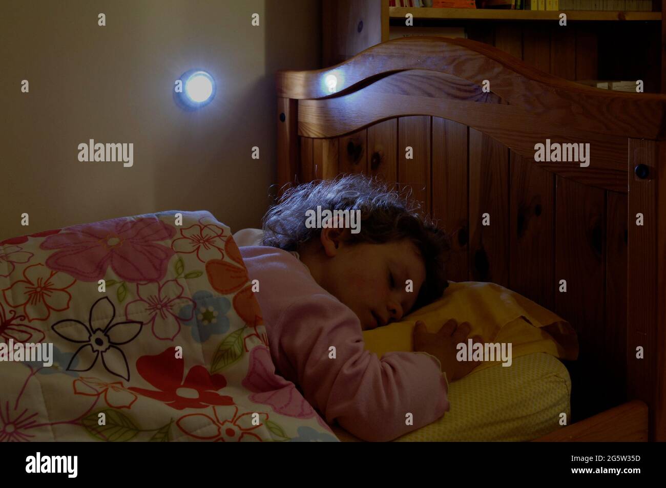 young girl afraid of the dark sleeping in a small cot bed with a night light next to the bed Stock Photo