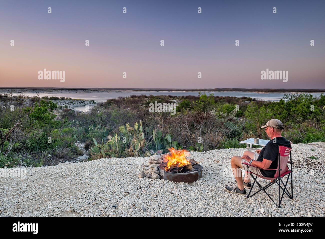 Camper sitting by fire, looking at Amistad Reservoir at sunset, Governors Landing campground, near Del Rio, Texas, USA Stock Photo