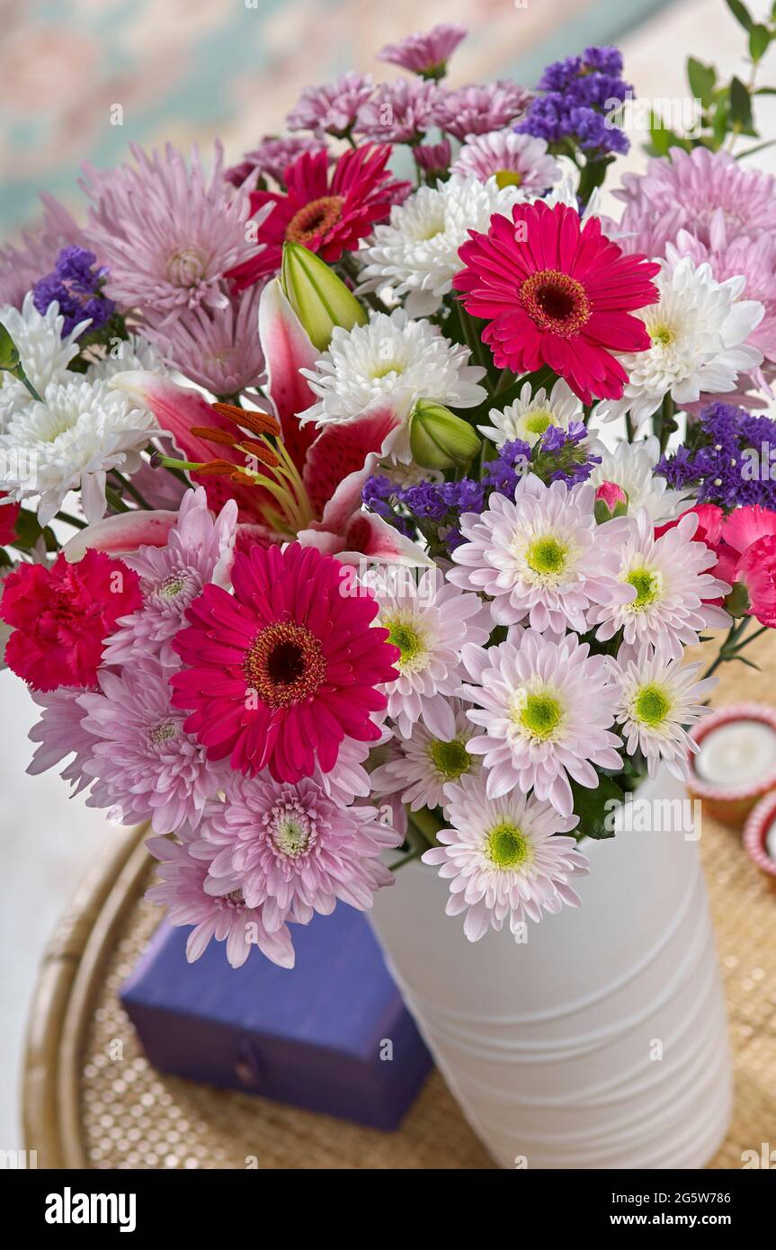 A large mixed bouquet of flowers in a vase on a small coffee table in a room setting Stock Photo