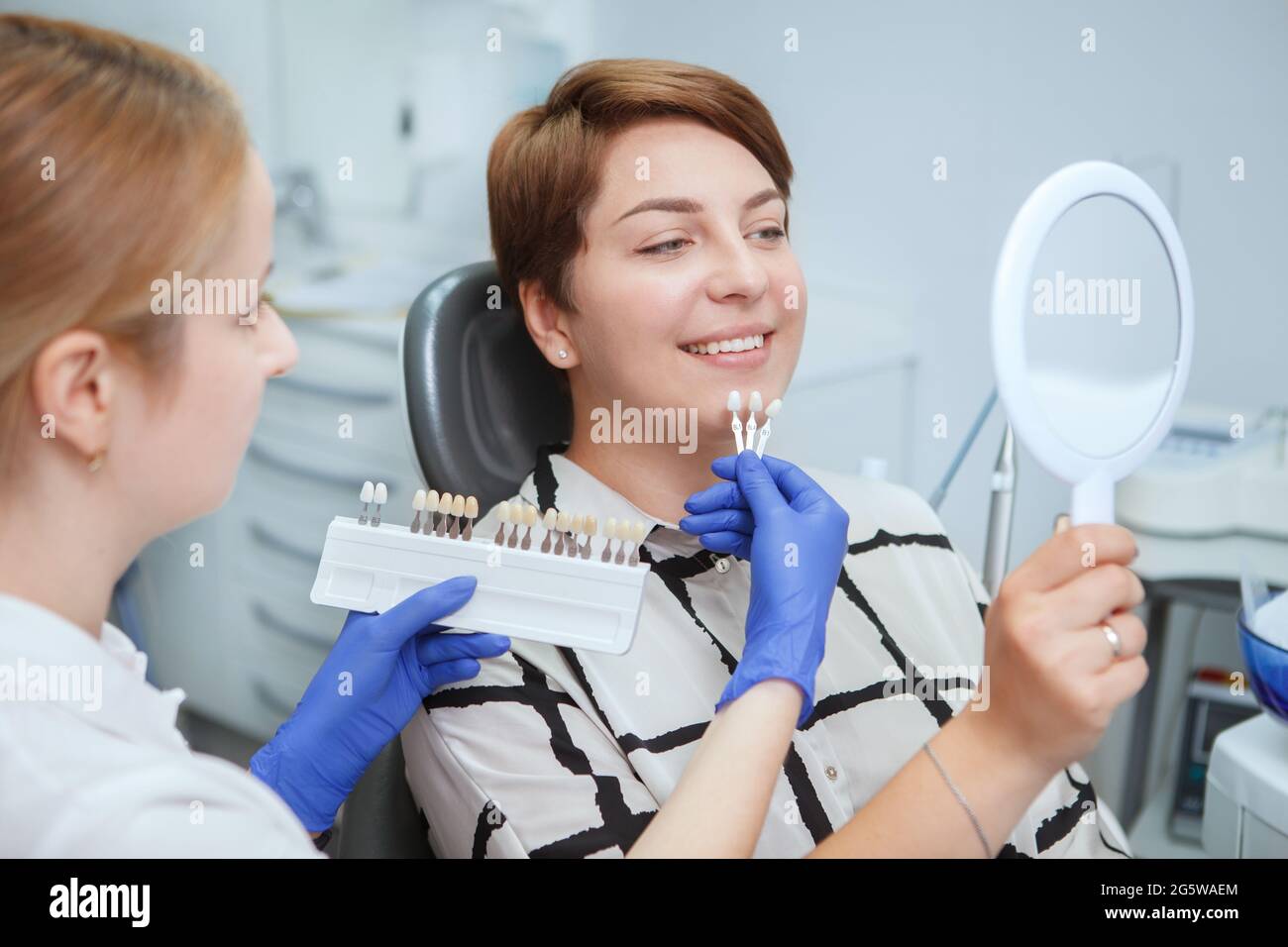 Dentist helping female patient pick teeth whitening shade from the chart Stock Photo