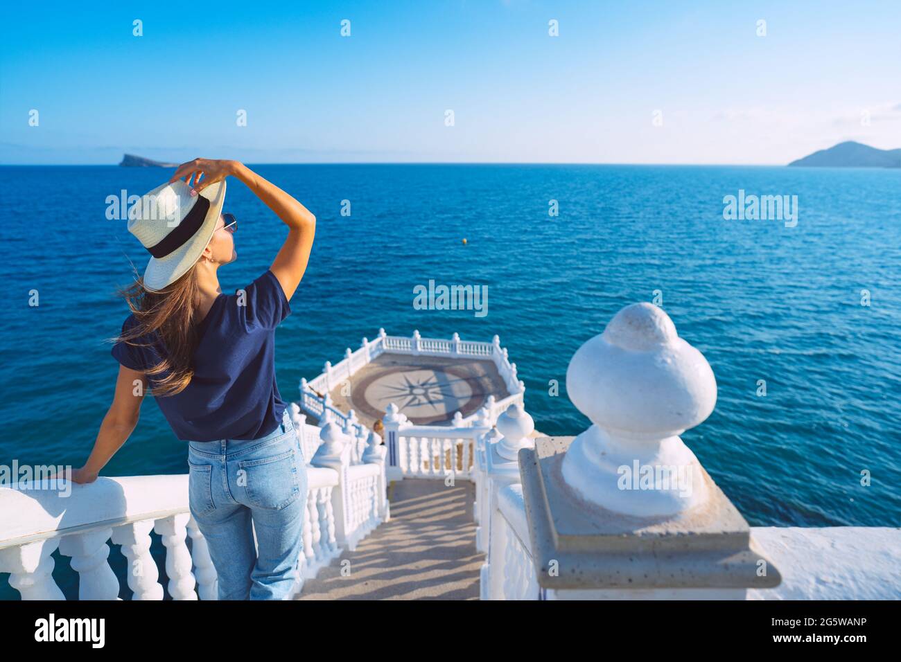 Young carefree tourist woman in white sun hat enjoying sea or ocean view in Balcon del Mediterraneo, Benidorm, Spain. Summer holiday vacation. Stock Photo