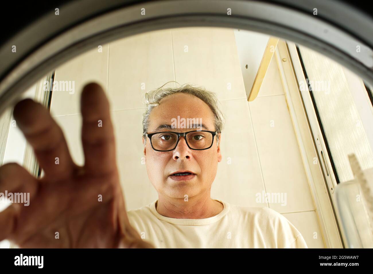 mature man taking clothes out of the washing machine seen from inside Stock Photo