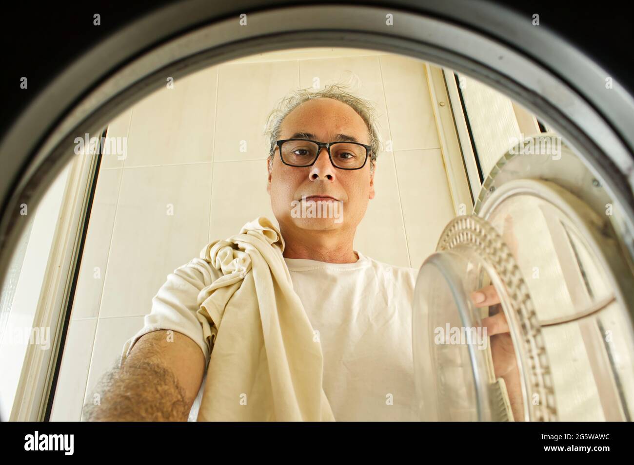 mature man taking clothes out of the washing machine seen from inside at home Stock Photo