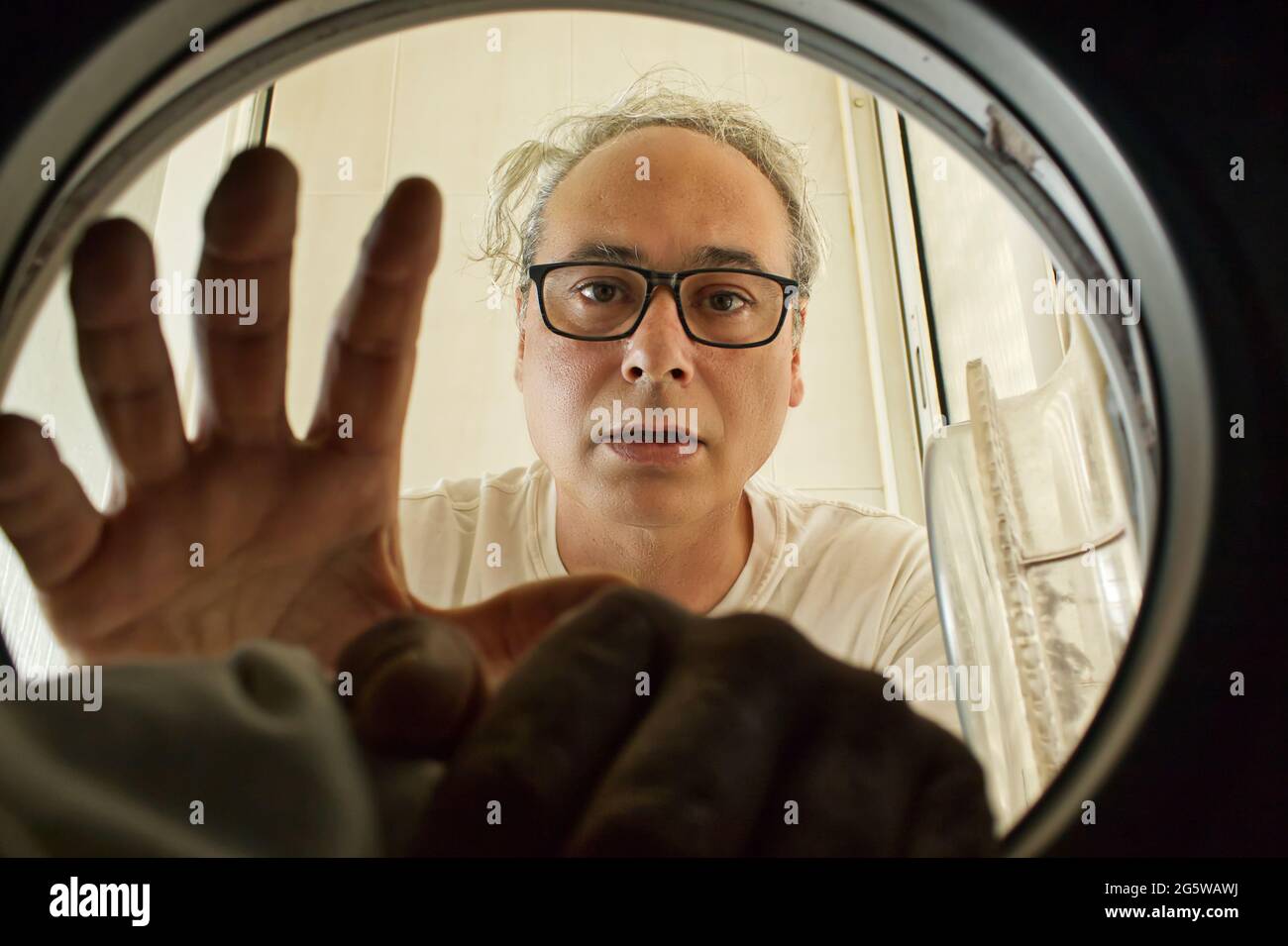 mature man taking clothes out of the washing machine seen from inside Stock Photo