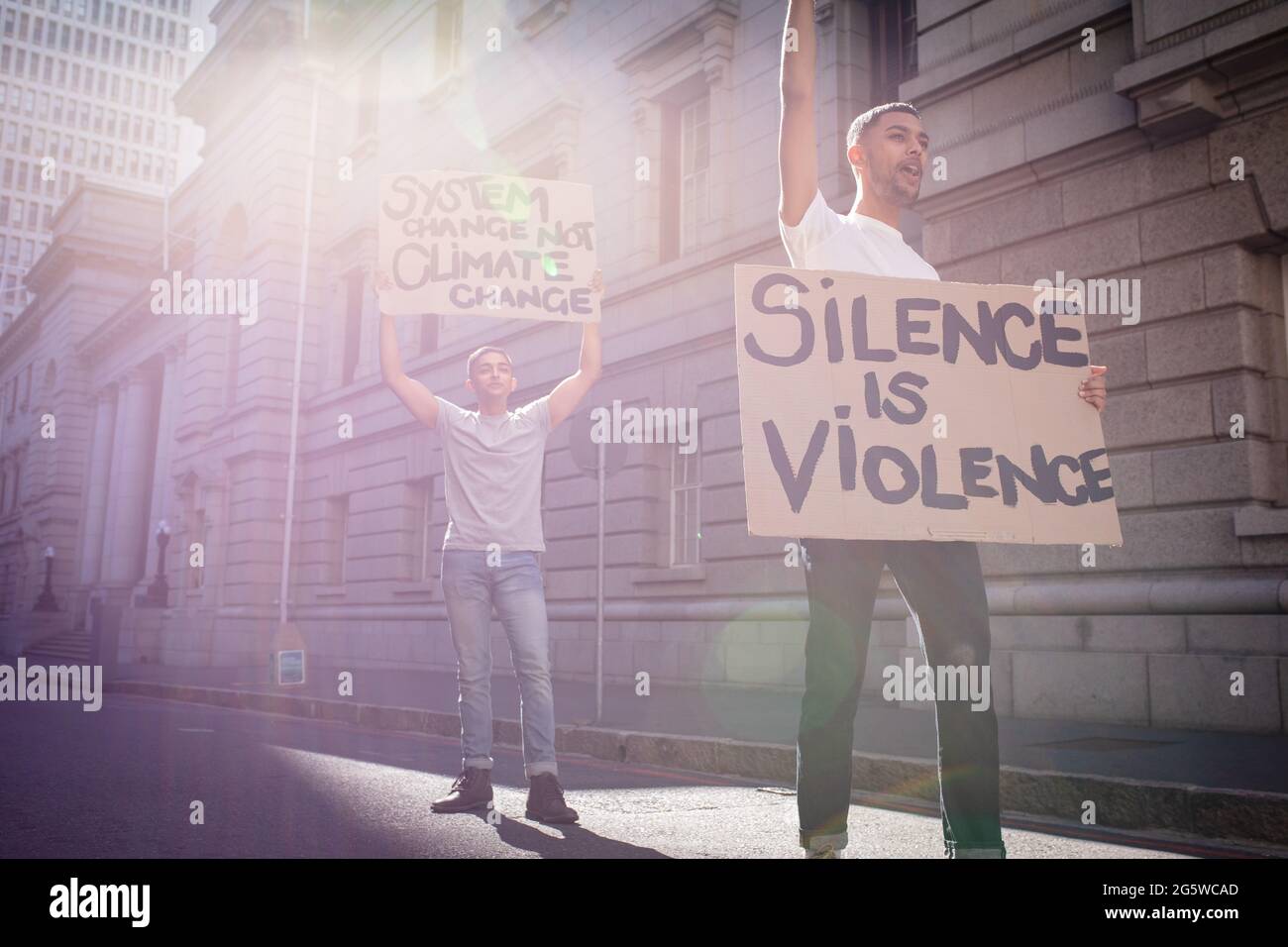 Two mixed race male friends carrying protest signs with slogans in sunny city street Stock Photo