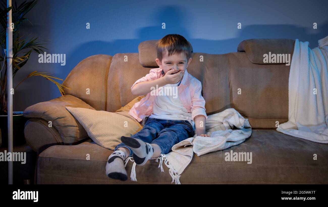 Happy little boy laughing on funny TV show or comedy movie at night Stock Photo