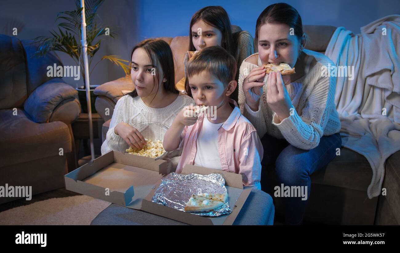 Big family watching late night TV show or movie on sofa and eating pizza and popcorn. Stock Photo