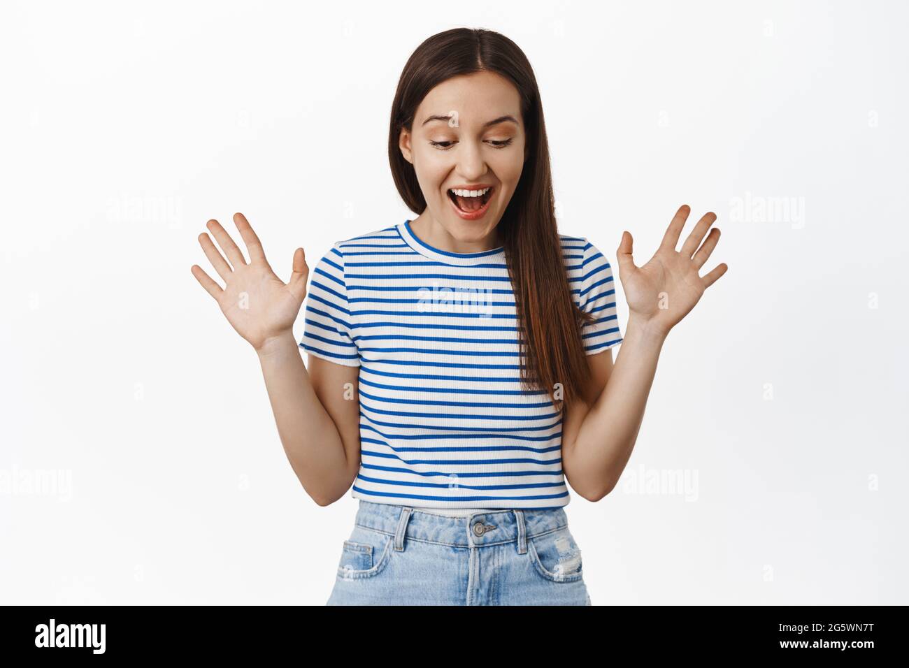 Image of surprised brunette girl smiles, looks in awe down, raise hands and rejoice, found sale promo below, staring at bottomg advertisement Stock Photo