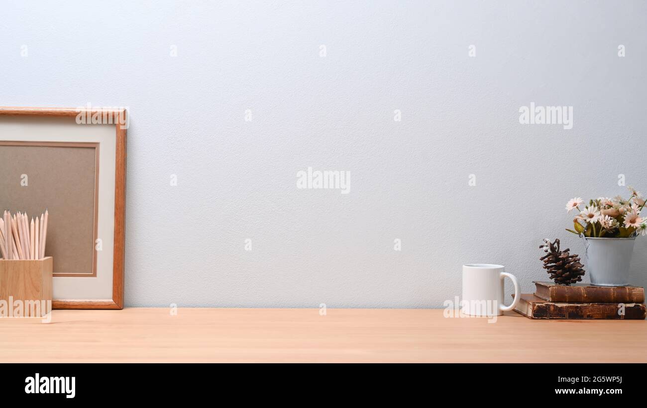 Contemporary workplace with empty frame, pencil holder, coffee cup and books on wooden table. Stock Photo