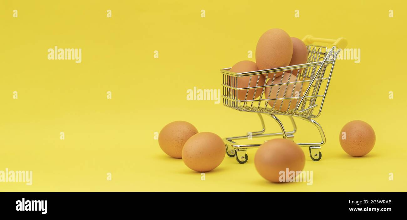 Raw chicken eggs in a basket on a yellow background. Eggs in a metal cart on a yellow background. Background with space for text Stock Photo