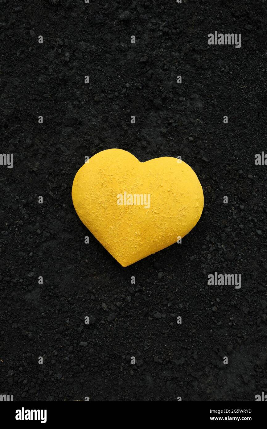 3 dimensional heart shape painted bright yellow with powder paint, placed on a background of black cinders Stock Photo