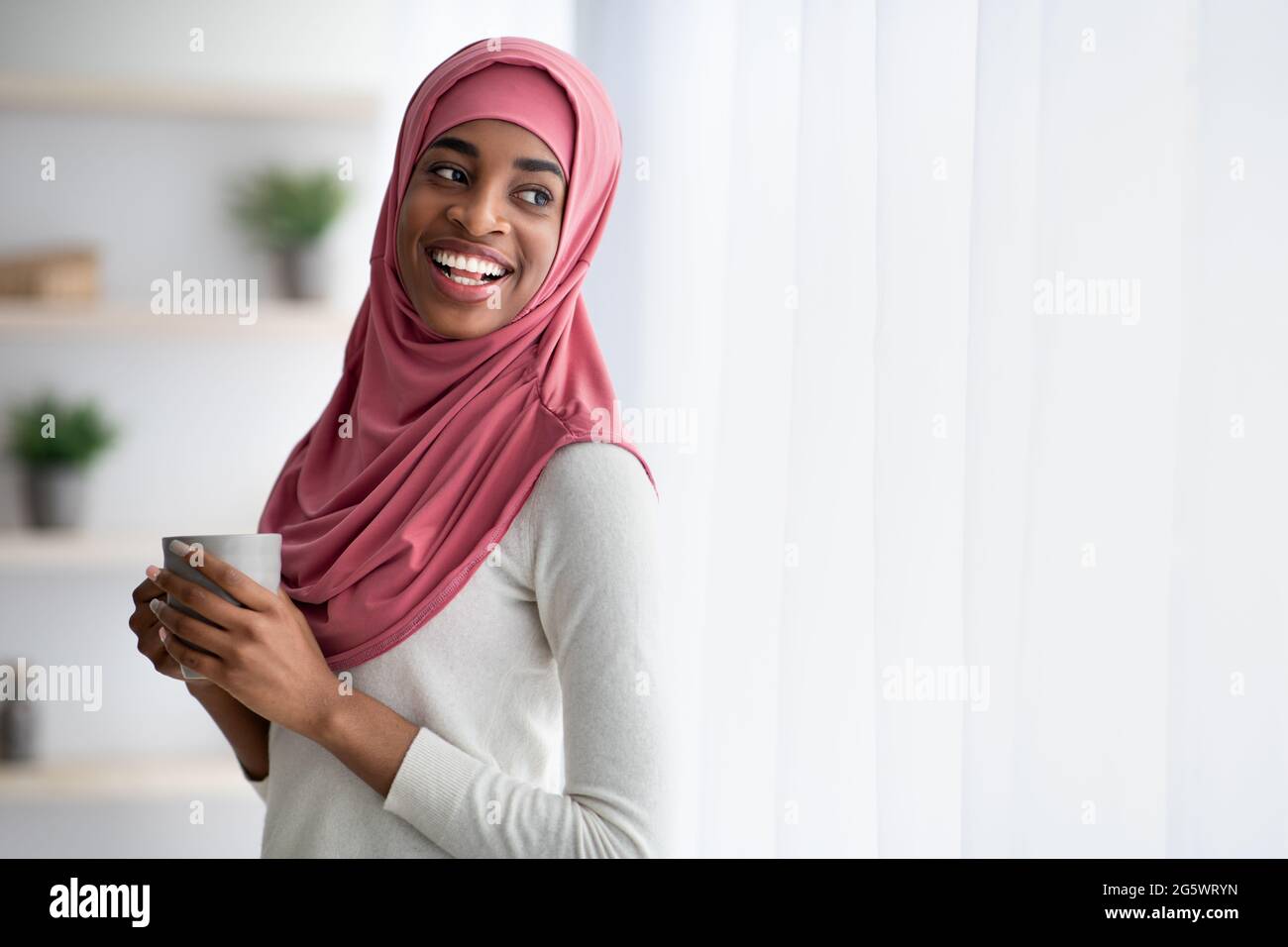 Happy Black Muslim Woman In Hijab Drinking Coffee Near Window At Home ...