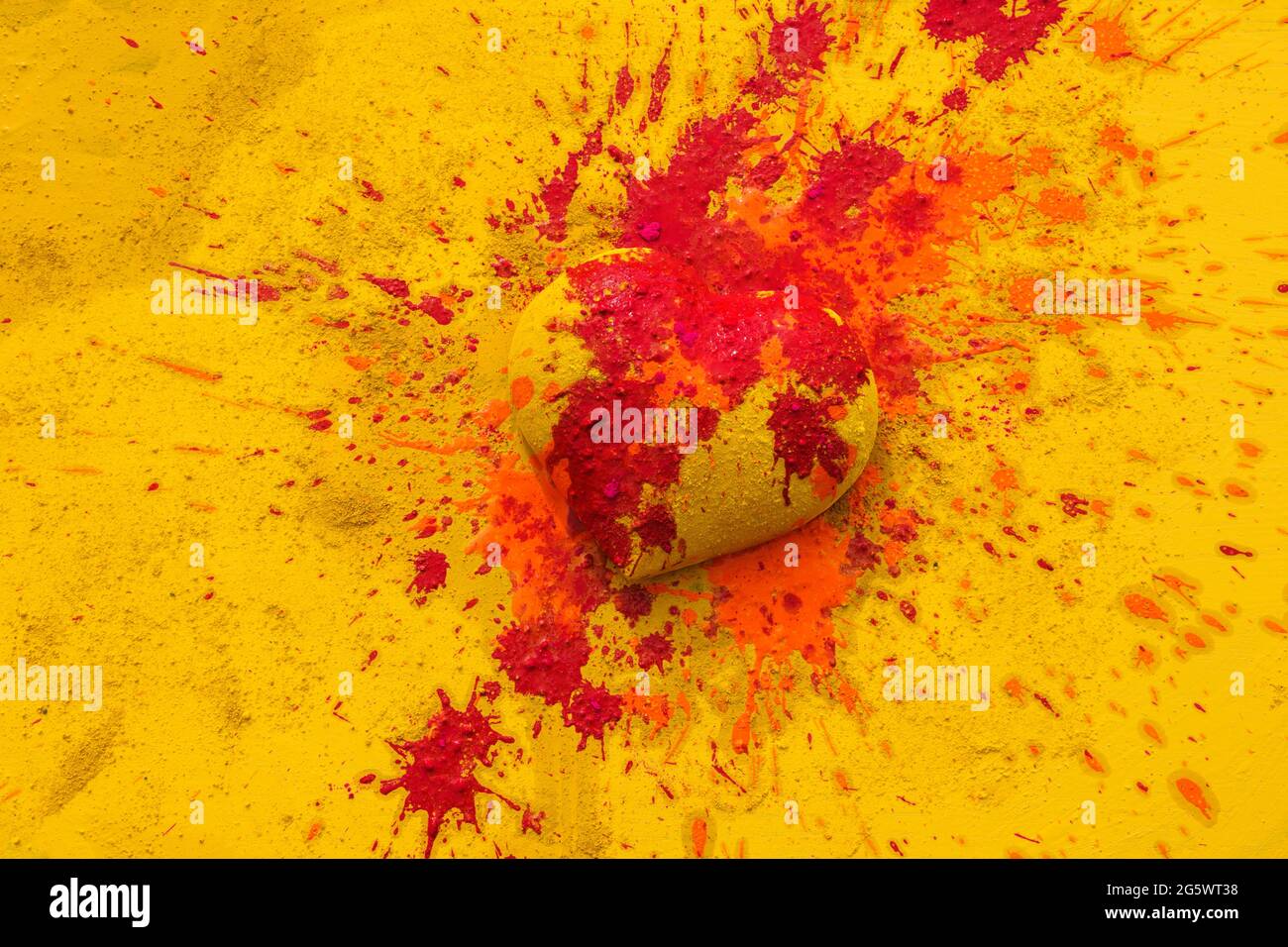 Yellow heart on yellow background splattered with orange and red paint. Stock Photo