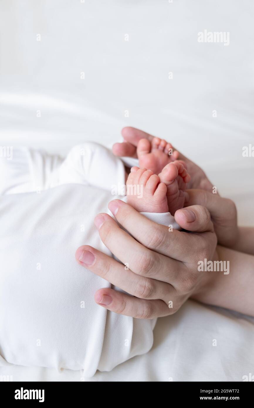 Mom and dad hands hold small legs of their two newborn twin babies